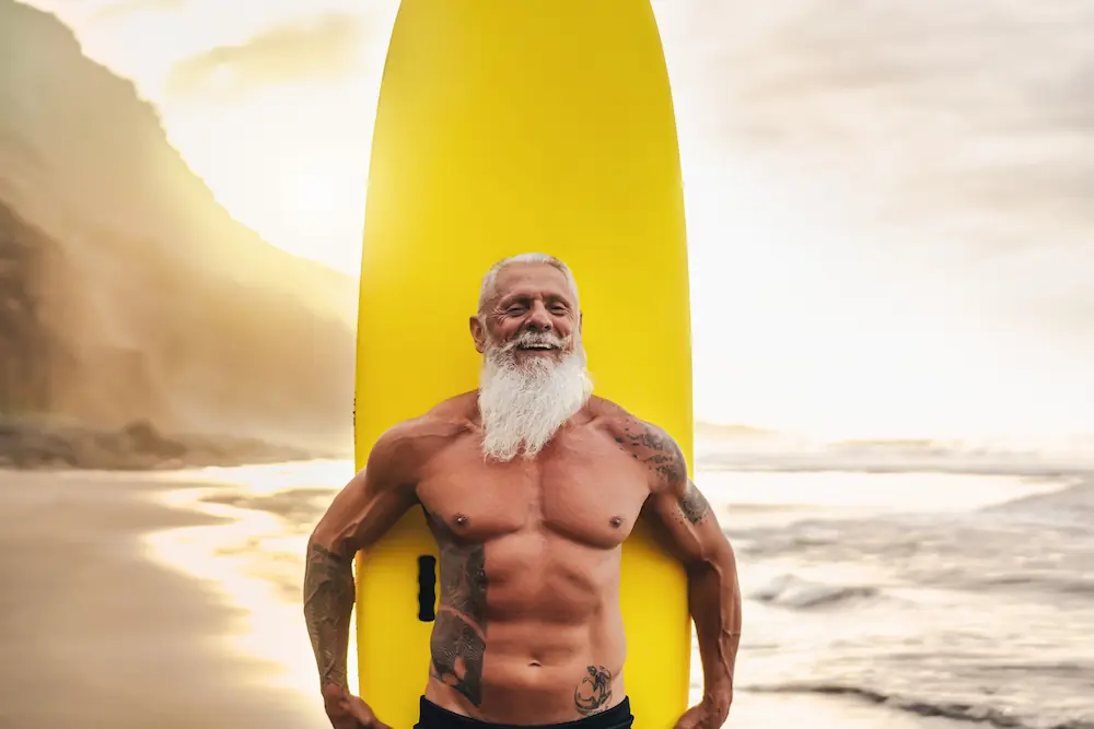 Smiling strong older man with a surfboard at the beach